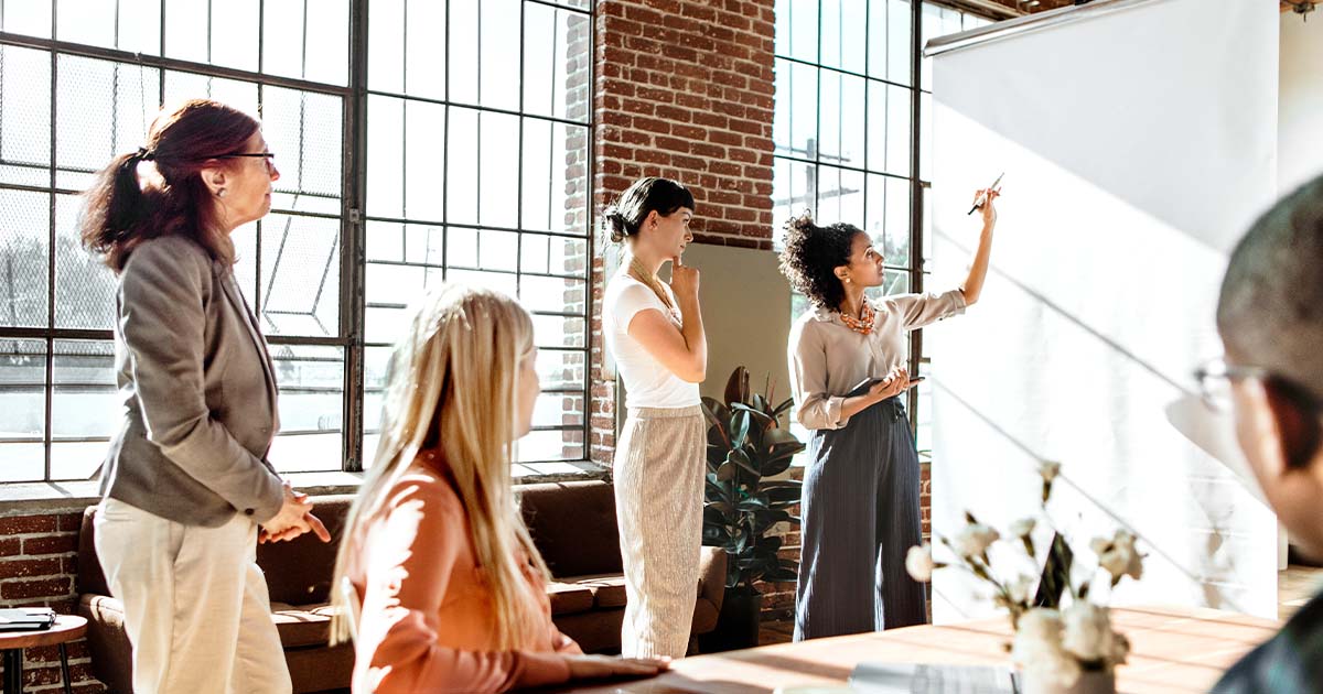 Lady at whiteboard talking in front of coworkers