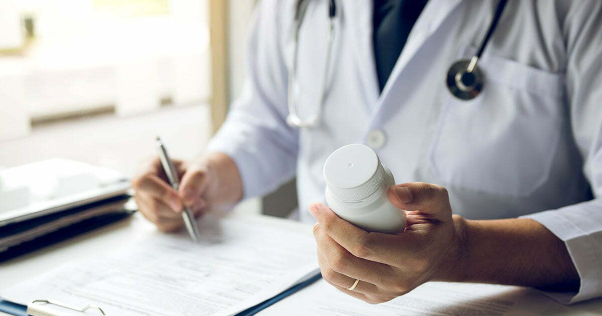 Doctor writing and holding bottle of pills