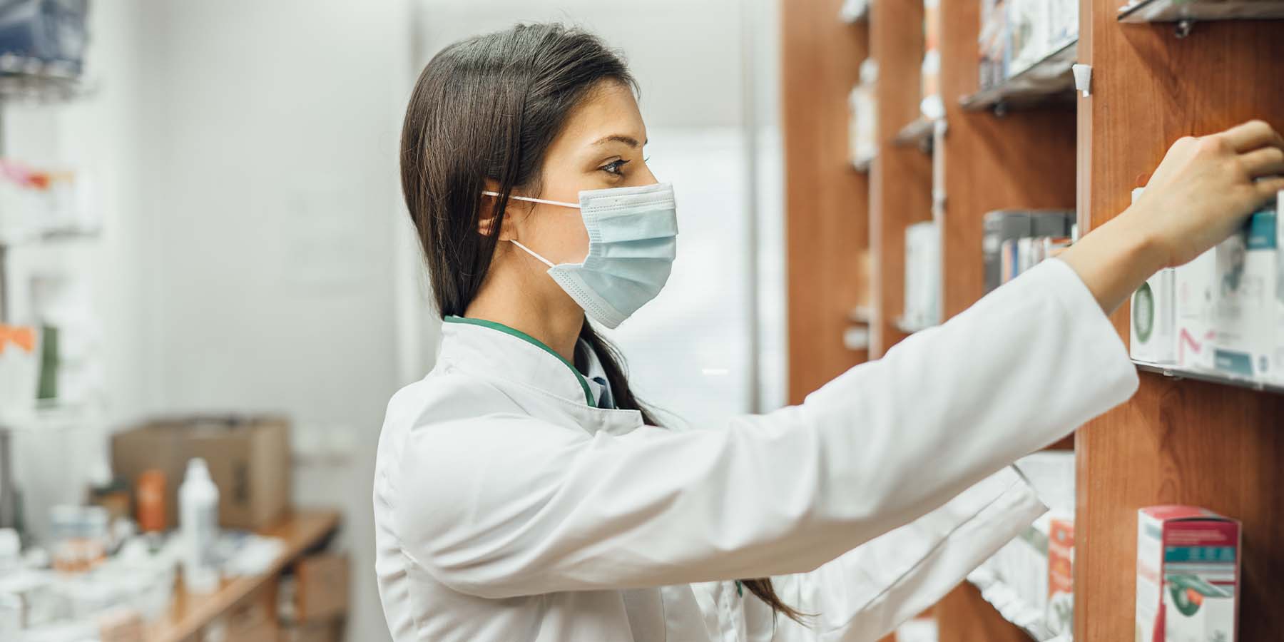 pharmacist grabbing medication while wearing a mask