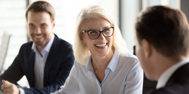 Happy business lady smiling at coworkers at table
