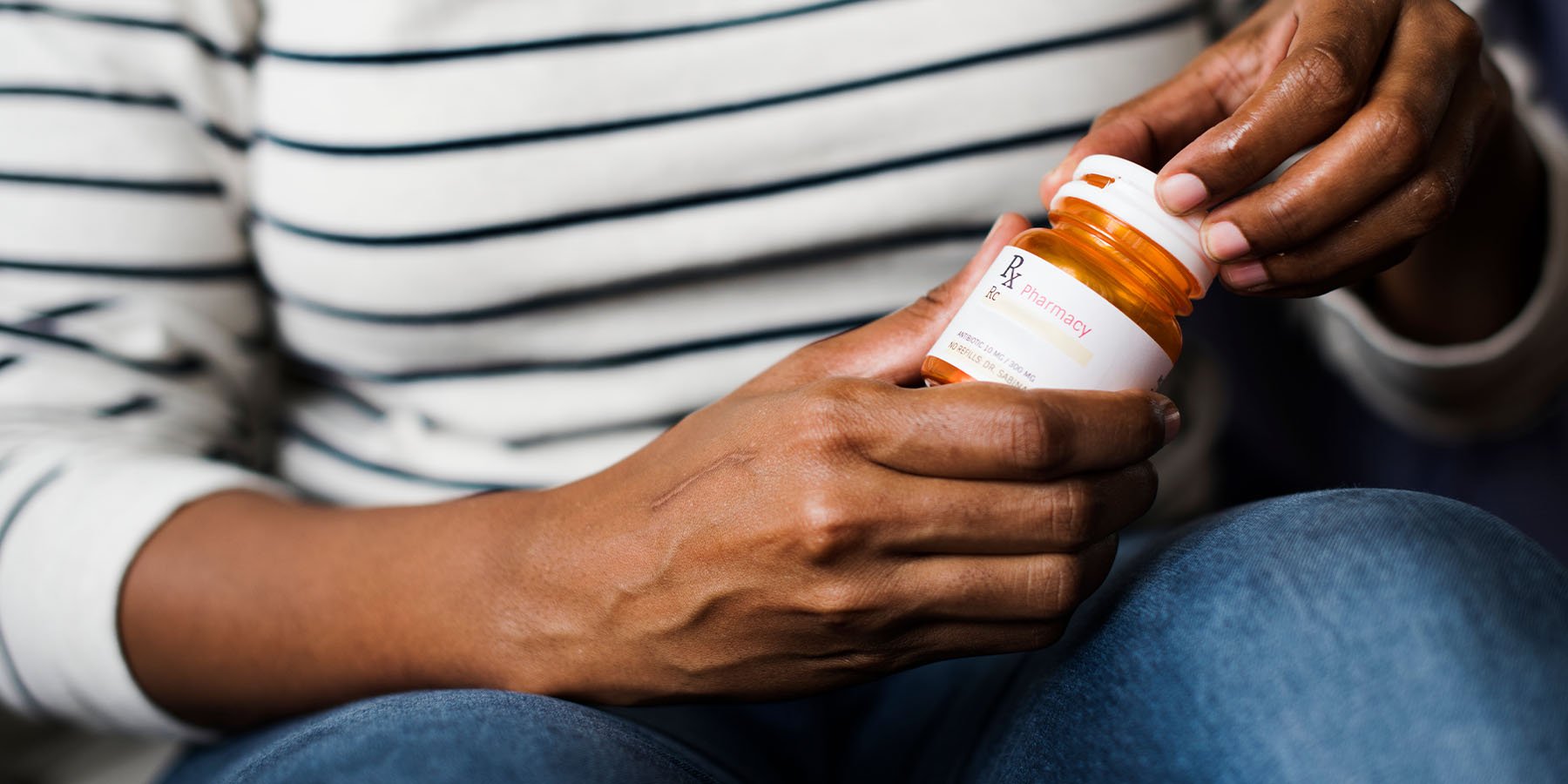 Lady sitting and opening an orange prescription bottle