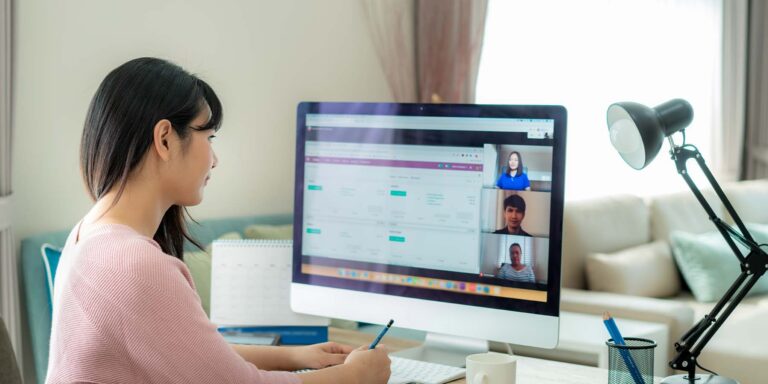 Lady taking notes with on an online meeting with coworkers