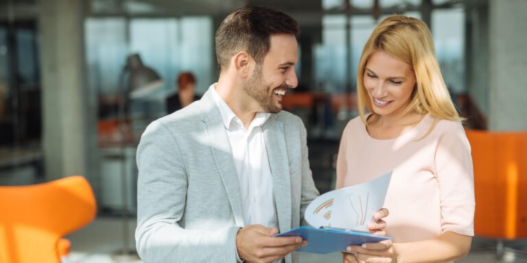 Two happy coworkers going over paperwork on a clipboard together