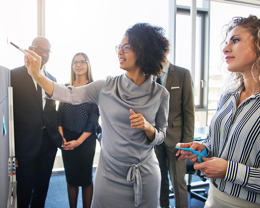 Business lady pointing at whiteboard and talking with coworkers