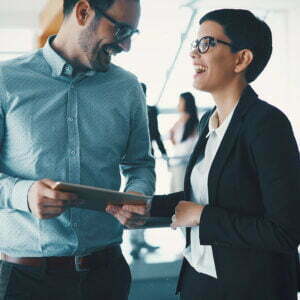 Two business people laughing and talking over something on an ipad they're looking at