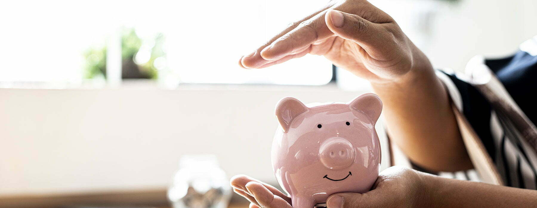 A person holding and putting a hand over a piggy bank to keep it safe