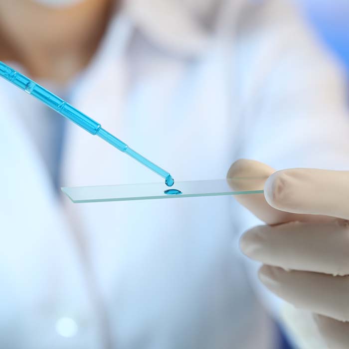 A scientist using a dropper to put blue liquid on a thing glass sheet