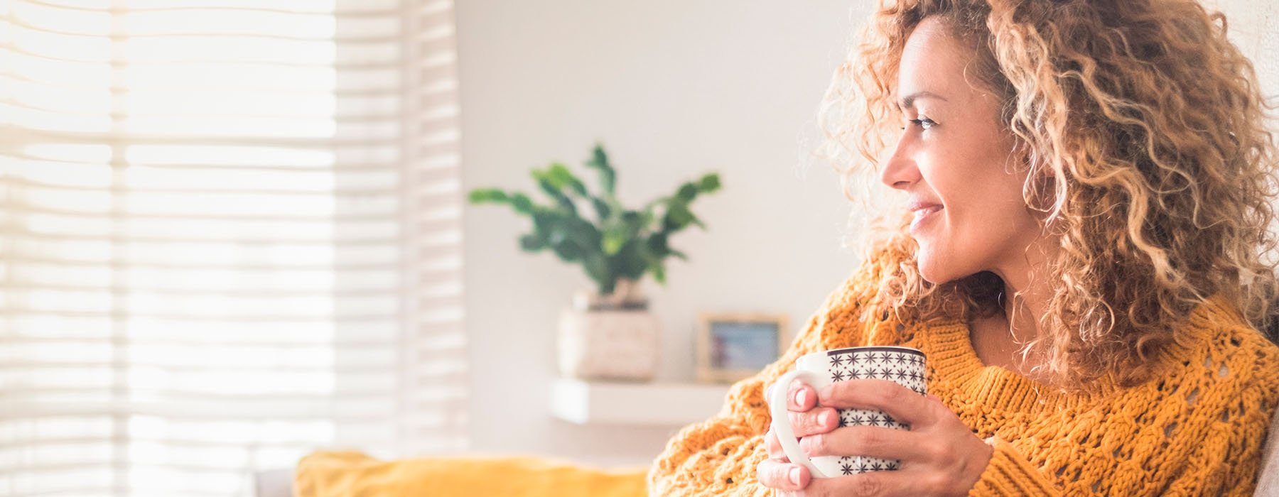 A lady in yellow sweater drinking coffee on couch and smiling