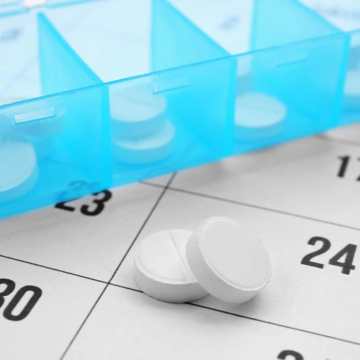A calendar that has a pill organizer on it and some loose pills outside the organizer