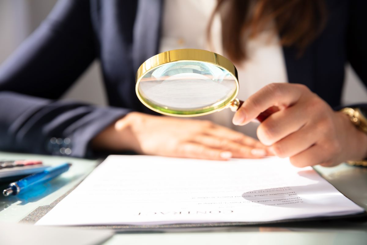 Business person reviewing contract with magnifying glass